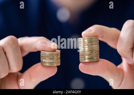 Man Holding Two Coin Stacks To Compare Stock Photo