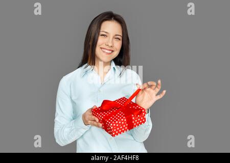 Freestyle. Young woman standing isolated on grey opening gift smiling happy Stock Photo