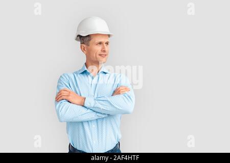 Construction. Mature man in hardhat standing isolated on white crossed arms looking aside pensive Stock Photo
