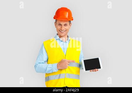 Construction. Mature man in hardhat and uniform standing isolated on white showing screen of digital tablet copy space smiling playful Stock Photo