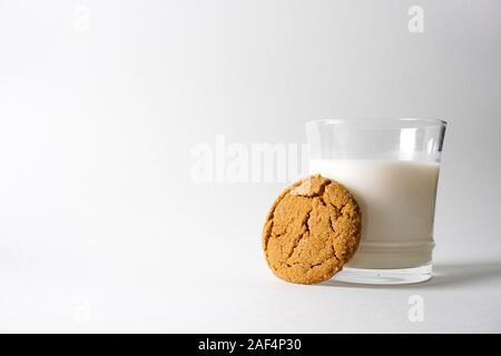 A gingerbread cookie leans up against a glass of cold milk on a white background with copy space on the left Stock Photo