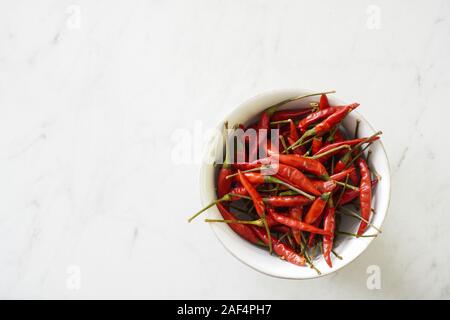 A white bowl of bright red Thai bird chiles on a marble cutting board with copy space; food preparation Stock Photo