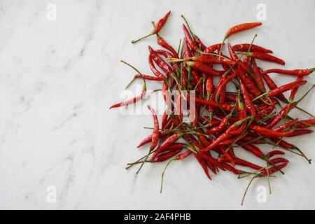 View from above of a pile of bright red Thai bird chiles on a white marble cutting board with copy space; food preparation Stock Photo