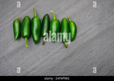 A row of green jalapenos peppers lined up on a gray slate cutting board; food preparation Stock Photo