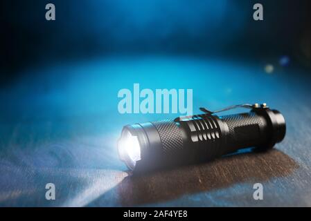 Tactical waterproof flashlight. LED flashlight shines on the table in smoke.. Stock Photo
