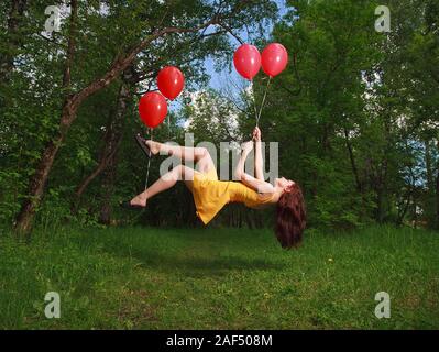 Adorable young brunette girl levitating on balloons in a park Stock Photo