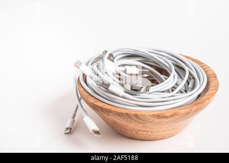 Several white Apple power cables and connectors swirling in a wooden bowl set on plain white background. Stock Photo