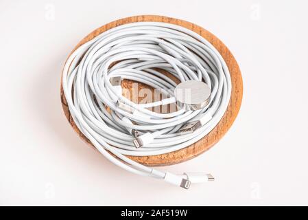 Several white Apple power cables and connectors swirling in a wooden bowl set on plain white background. Stock Photo