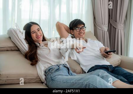 Asian couple lifestyle, man holding remote control and woman watching TV movies at home, family lifestyle relax and recreation concept. Stock Photo
