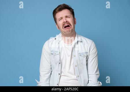 Funny caucasian man crying wipes tears losing his job. Studio shot on blue background. Stock Photo