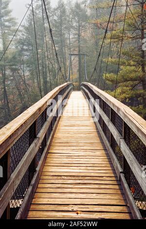 Modern suspension bridge crossing over the Tallulah River at Tallulah Falls Georgia USA. A nearby wildfire creates a hazy atmosphere. Stock Photo
