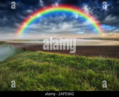 rainbow in the field. picturesque sky over a hilly field. after a thunderstorm Stock Photo
