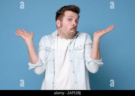 Confused caucasian man is unsure in studio shrugging shoulders up. I do not take your money. Studio shot Stock Photo