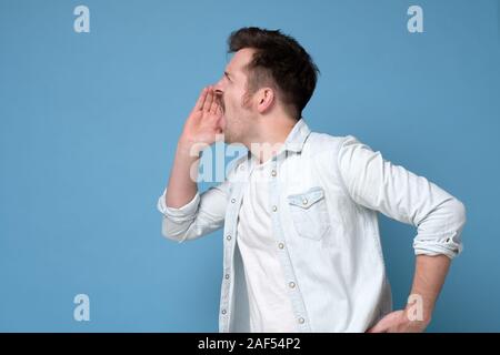 Handsome young man calling someone or making announcement isolated over a blue background Stock Photo