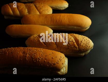 Freshly baked loaf of fresh breads on black background. Hotdog breads and others. Stock Photo