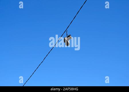 An old pair of men's sneakers hanging on wires against a blue sky. Torn black sneakers on a wire. Stock Photo