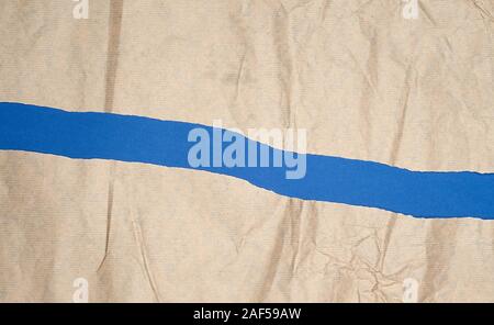 torn brown sheet of paper on a blue background, full frame, close up Stock Photo