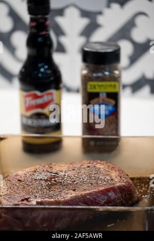 A raw rib eye steak marinating in Worcestershire sauce and dry steak seasoning for flavor and tenderness before cooking. Looking down. USA. Stock Photo