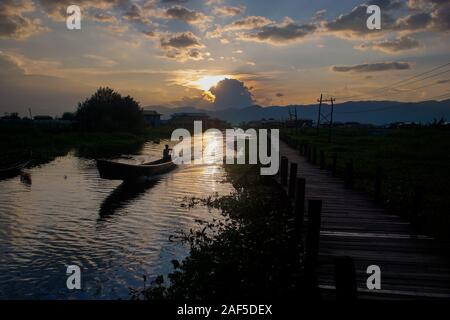 A boat travels down the canal next to the long wooden bridge at Maing Thauk village in Inle Lake in Myanmar (Burma) Stock Photo