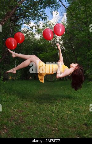 Adorable young brunette girl levitating on balloons in a park Stock Photo