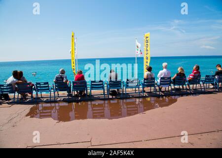 People sitting on the Promenade des Anglais taking in the views of the beach and sea in Nice France Stock Photo