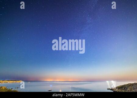 Long exposure of Mgiebah Bay in Malta on a clear summer night.  Street lights from Sicily can be clearly seen in the background on the horizon. Stock Photo