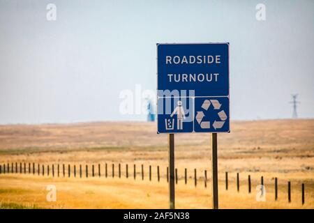 Information Road blue Sign, Roadside turnout with Tidy man and Recycling symbols on Canadian rural country roadside against yellow prairies and plains Stock Photo