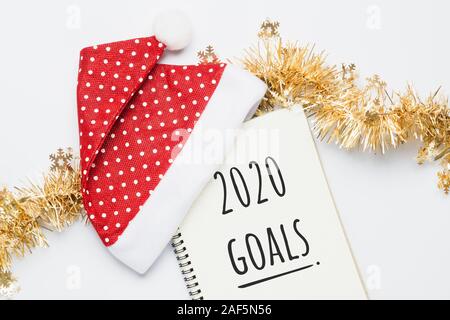 2020 New Year, Goals. Santa Hat with white Notebood. 2020 GOALS Text on paper on white background. Top view Flat lay Stock Photo