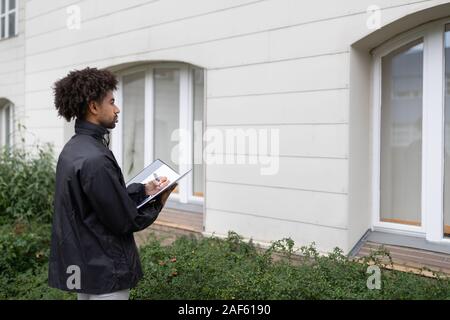 Close-up Of A Person's Hand Filling Document In Front Of House Stock Photo