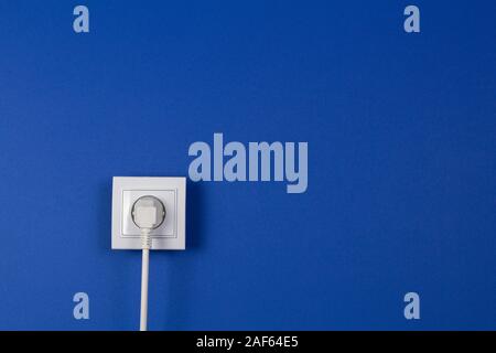 White cable plugged into electrical socket on blue navy color background Stock Photo