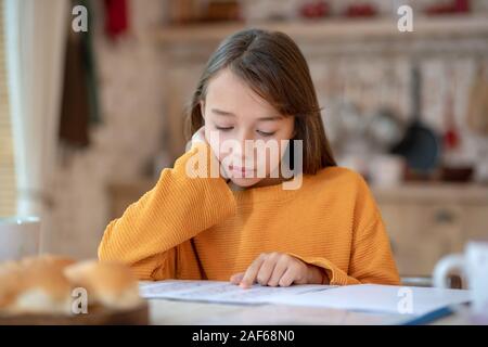 Cute girl in orange shirt looking concentrated Stock Photo