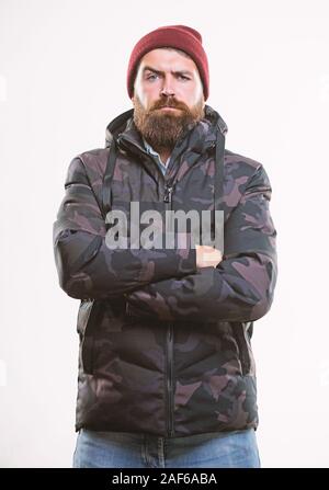 Comfortable winter outfit. Winter stylish menswear. Man stand warm camouflage pattern jacket parka with hood isolated on white background. Guy wear hat and black winter jacket. Hipster winter fashion. Stock Photo