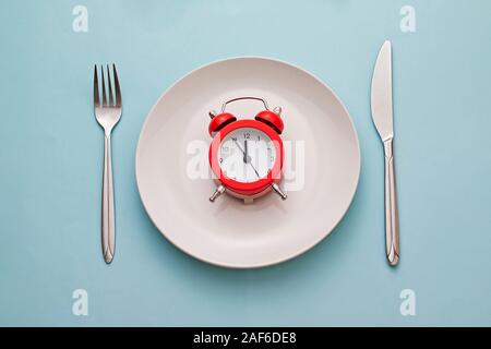 Red alarm clock on a clean white dinner plate Stock Photo