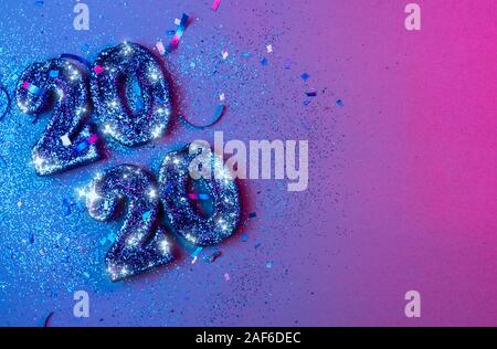 New years 2020 3d numbers flat lay with confetti and christmas bulbs lit by vivid blue and pink lights - new years holiday concept image with copy spa Stock Photo