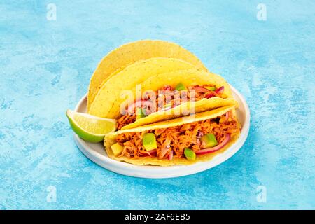 Cochinita pibil taco shells, a Mexican snack with pulled pork and avocado and marinated red onion, a close-up shot on a blue background Stock Photo