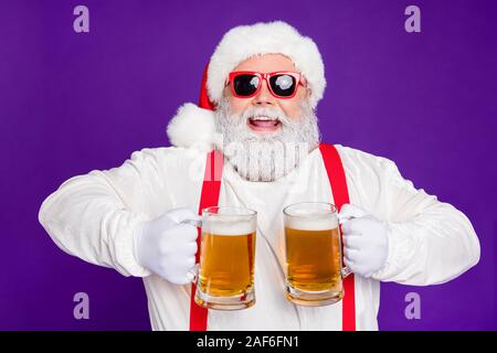 Close-up portrait of nice glad cheerful cheery positive bearded Santa holding in hands two mugs drinking beer having fun isolated over bright vivid Stock Photo