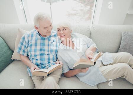 Above high angle view of her she his he two nice attractive cheerful cheery spouses sitting on divan reading new interesting funny book in light white Stock Photo