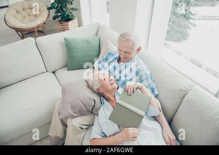 Above high angle view of her she his he two nice cheerful cheery positive spouses sitting lying on cosy divan reading interesting book in light white Stock Photo