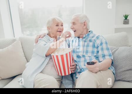 Portrait of two nice attractive funny cheerful cheery positive spouses having fun spending free time watching cinema in light white interior living Stock Photo