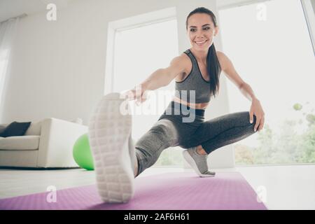 Full size photo of joyful active athlete girl want be strong sportswoman practice aerobics warm-ups sit on violet mat do squats stretch legs touch Stock Photo