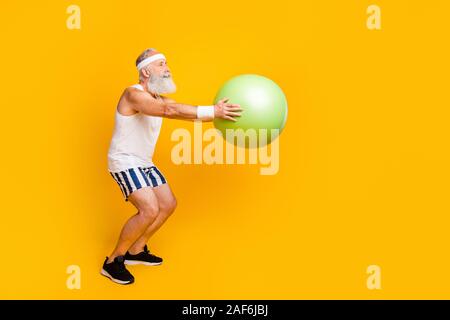 Full length profile photo of aged guy hold green fit ball doing squats serious fat burning sportswear tank-top shorts sweatband sneakers isolated Stock Photo