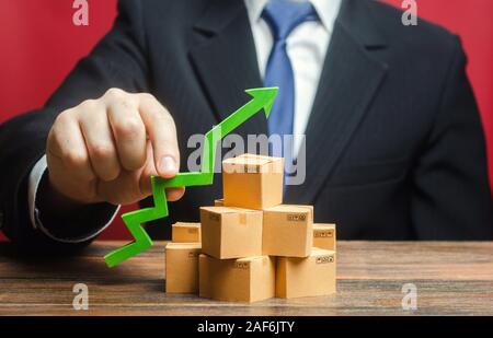 Businessman holding a green arrow up over boxes. Boost sales rate. Increasing production of goods, expanding export opportunities, finding markets. Ta Stock Photo
