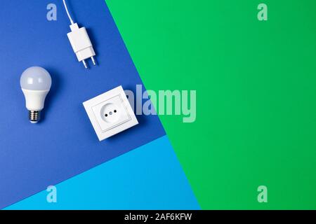 White electrical power socket, power plug, light lamp bulb on light blue, navy and green background. Top view Stock Photo