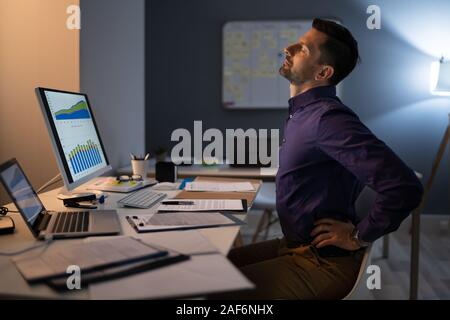 Young Businessman Having Back Pain While Sitting At Office Desk Stock Photo