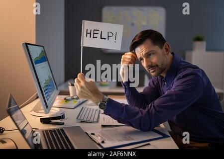 Businessman Holding Help Flag Over The Desk At Workplace Stock Photo