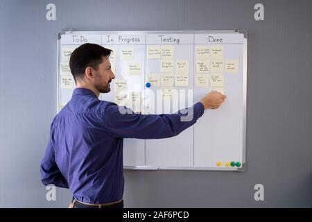 Side View Of Businessman Writing On Sticky Notes Attached To White Board In Office Stock Photo