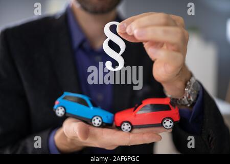 Lawyer Holding Two Small Cars In Hand And Paragraph Sign Stock Photo