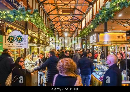 Mercado San Miguel in Madrid, Spain is busy with people. An indoor market seen here in December with festive Christmas garlands decorating the beams. Stock Photo