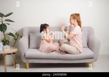 Happy young woman playing clapping game with female child while sitting in livingroom Stock Photo