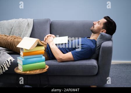 Man Sleeping On Sofa At Home With Book Stock Photo